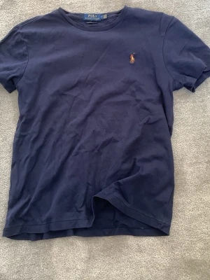 Mörkblå t-shirt från Polo Ralph Lauren - Klassisk mörkblå t-shirt från Polo Ralph Lauren med broderad logga på bröstet. T-shirten har rund halsringning och korta ärmar. Tillverkad i mjuk bomull för en skön och avslappnad stil.