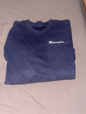 Mörkblå Champion sweatshirt - Mörkblå sweatshirt från Champion med klassisk logga broderad på bröstet. Tröjan har rund halsringning och är tillverkad i mjukt bomullsmaterial. Perfekt för en avslappnad och sportig stil.