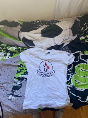 Vit t-shirt med stor logga - Vit t-shirt  med stor broderad logga framtill i blått och rött. Klassisk rund hals och korta ärmar. Perfekt för dig som gillar stilrena och exklusiva plagg med tydlig branding.
