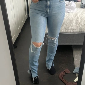 Ljusblå slitna jeans med hög midja - Säljer ett par ljusblå jeans med hög midja och raka ben från Zara. Jeansen har stora slitningar vid knäna och råa, fransiga benslut. Perfekta för en avslappnad och trendig look.