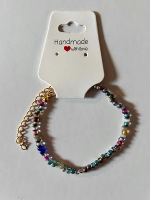 Färgglatt pärlarmband med guldkedja - Ett handgjort armband med små, färgglada pärlor i olika nyanser och en justerbar guldfärgad kedja. Perfekt accessoar för att addera lite färg till din stil. Armbandet är lätt och smidigt att bära.