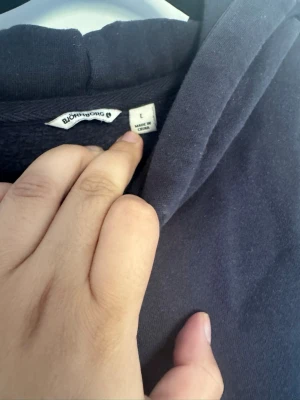 Mörkblå hoodie från Björn Borg - En stilren mörkblå hoodie från Björn Borg med huva och dragsko. Hoodien har en avslappnad passform och är tillverkad i mjukt material, perfekt för en chill och bekväm look. Liten logotypdetalj nertill på framsidan.