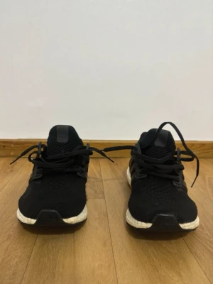 Svarta Adidas Ultra Boost  - Svarta Adidas Ultra Boost sneakers med stickad ovandel och klassiska tre ränder på sidan. Skorna har vit Boost-sula för extra komfort och svart yttersula. Perfekta för en sportig och stilren look.