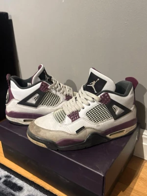 Air Jordan 4 PSG - Snygga Air Jordan 4 PSG Bordeaux sneakers i vitt, svart och vinrött med meshpaneler och ikoniska detaljer. Paris Saint-Germain collab med Jumpman-logga på plösen och PSG-märke på hälen. Skorna har en chunky sula och coola kontrastdetaljer.