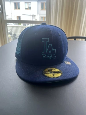 Blå LA Dodgers keps från New Era - Snygg blå keps från New Era med LA Dodgers-logga broderad framtill i turkos. Klassisk 59FIFTY-modell med platt skärm och broderad MLB-logga bak. Perfekt för dig som gillar streetwear och sportig stil.