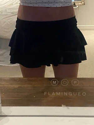 Svart och vit volangkjol - Två korta kjolar i svart och vitt med stretchig midja och flera lager volanger med shorts under till. Kjolarna har en feminin och lekfull stil, perfekta för att skapa en trendig look. Materialet är av polyester känns mjukt och följsamt. 