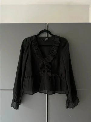 Svart volangblus  - Svart blus med volang från H&M. I mycket bra skick! (Den röda ”fläcken” på andra bilden är endast ljus som speglar sig, ej något på tröjan!) 
