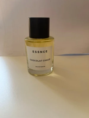 ESSNCE Chocolat Chaud Eau de Parfum - Parfymflaska från ESSNCE med doften Chocolat Chaud. Flaskan är cylindrisk i genomskinligt glas med svart lock och vit etikett. Innehållet är ljusgult. En stilren och modern parfym som sticker ut med sin chokladdoft. Flaskan rymmer 30ml och är inte använd. Hör av er vid minsta lilla fråga och priset kan diskuteras vid snabb affär.