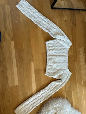 NAKD Vit kabelstickad cropped tröja - Trendig vit kabelstickad cropped tröja med långa ärmar och rund hals. Perfekt för lager-på-lager och passar till både jeans och kjol. Mjuk och skön stickning i ett klassiskt mönster.
