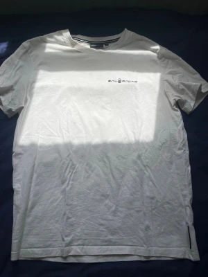 Vit t-shirt från Sail Racing - Vit t-shirt från Sail Racing med diskret logga på bröstet och en liten logga i nacken. Klassisk passform och rund halsringning. Perfekt basic-plagg att ha i garderoben.