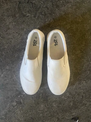 Vita slip-on sneakers i canvas - Stilrena vita slip-on sneakers i canvas med elastiska paneler på sidorna för enkel på- och avtagning. Klassisk låg modell med vit sula och minimalistisk design som passar till det mesta. Perfekta för en avslappnad och trendig look.