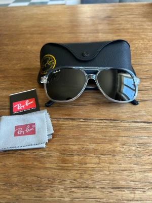Ray-Ban bill - Snygga Ray-Ban Bill solglasögon med transparent båge och svarta glas. Klassisk design med svarta skalmar och Ray-Ban-logga på linsen. Kommer med originalfodral och putsduk. Perfekt accessoar för en cool look.