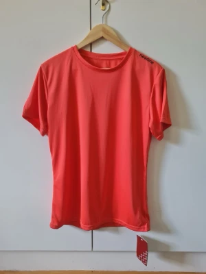 Korallröd tränings t-shirt från Newline strl XL EUR 44 dam - Korallröd tränings t-shirt från Newline med rund hals och korta ärmar. Storlek XL / EUR 44 dam. Nyskick med etiketter som sitter kvar.