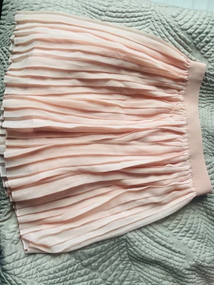 Plisserad ljusrosa kjol från NA-KD - Supersöt plisserad kjol från NA-KD i en ljusrosa nyans. Kjolen har resår i midjan och är kort i modellen, perfekt för en trendig och feminin look. Tillverkad i ett lätt och luftigt material som ger snyggt fall.
