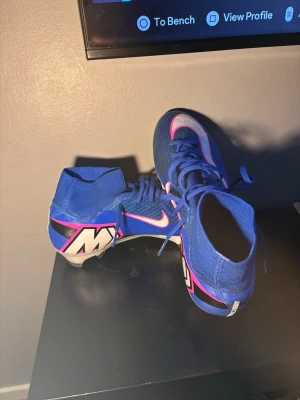 Nike Air Zoom Mercurial blå fotbollsskor - Nypris 3000 använda en gång passar inte min fot därför jag säljer dom.         Säljer ett par Nike Air Zoom Mercurial fotbollsskor i blått med rosa och vita detaljer. Skorna har hög krage för extra stöd, snörning och en lätt sula med dobbar för bra grepp på planen. Perfekta för dig som vill sticka ut på matchen!
