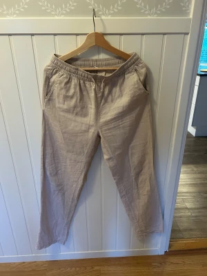 Beige linnebyxor med resårmidja - Snygga beige linnebyxor med avslappnad passform och resår i midjan. Byxorna har snedställda fickor och är tillverkade i ett lätt och luftigt linnematerial, perfekta för en chill och stilren look.