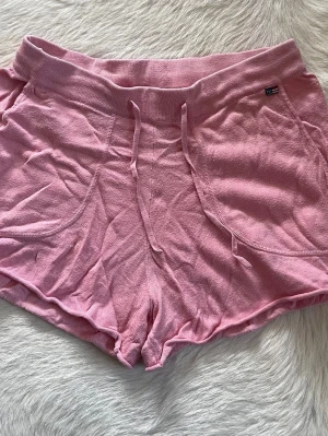 Rosa frotté-shorts från Lexington med snörning i storlek S  - Säljer ett par rosa frotté-shorts från Lexinton med bred resår i midjan och snörning framtill. Storlek S. Shortsen har två stora fickor och är gjorda i ett mjukt bomullsmaterial. Perfekta för chill dagar eller träning.