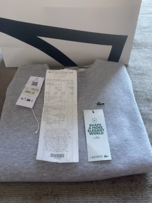 Grå sweatshirt från Lacoste - Snygg grå sweatshirt från Lacoste med klassisk krokodillogga på bröstet. Tröjan har rund halsringning och är tillverkad i mjukt material som passar perfekt till en avslappnad stil. Tröjan är använd få tal gånger.