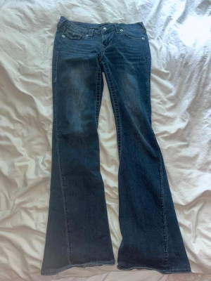 Mörkblå bootcut jeans. - Original pris: 1100kr. Blåa bootcut jeans från true religion i designen Joey storlek 26. Dem är använda några gånger och har tyvärr trampat upp dem lite längst ner men inget så syns så mycket. Ena fickan har böjt sig lite men de går att  eneklt fixa med strykjärn. 