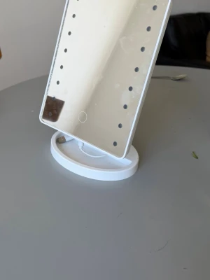 Vit sminkspegel med LED-belysning - Snygg vit sminkspegel med rektangulär form och inbyggda LED-lampor runt spegeln. Spegeln har touchknapp på framsidan och laddas via USB-kabel som medföljer. Perfekt för att fixa sminket med bra ljus. Står stadigt på en rund fot.