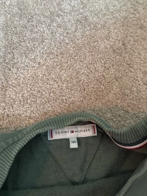 Grön stickad tröja Tommy Hilfiger - Snygg grön tröja från Tommy Hilfiger med rund halsringning och logga broderad framtill. Tröjan har ribbade muddar vid ärmslut och nederkant samt klassisk passform. Perfekt för dig som gillar stilrena och bekväma plagg.