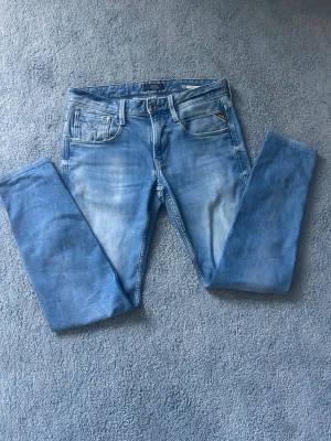 Ljusblå slim fit jeans från replay - Snygga ljusblå slim fit jeans från Jack & Jones med klassisk femficksdesign och diskreta slitningar framtill. Jeansen har normal midja och är tillverkade i bomull med lite stretch för extra komfort. Perfekta för en avslappnad och trendig look.