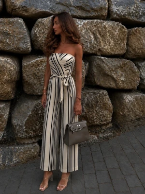 Randig bandeau jumpsuit med knytskärp - Snygg vit jumpsuit med svarta vertikala ränder och bandeau-överdel. Vida ben och knytskärp i midjan ger en trendig och avslappnad look. Perfekt för dig som vill sticka ut med stilrena detaljer. Materialet känns lätt och luftigt.