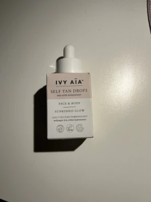 IVY AIA Self Tan Drops Sunkissed Glow - IVY AIA Self Tan Drops Sunkissed Glow är brun-utan-sol-droppar för ansikte och kropp. Kommer i en vit och beige förpackning med pipett, vegansk och parfymfri formula. Blandas med din vanliga ansiktskräm för en naturlig solkysst look.