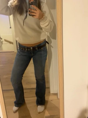 Blå bootcut jeans från True Religion - Säljer ett par blå bootcut jeans från True Religion med klassiska kontrastsömmar och detaljerade bakfickor. Jeansen har låg midja och är tillverkade i denim med lätt stretch. Perfekta för dig som gillar en avslappnad men snygg stil.