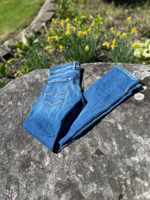 Replay Grover Jeans - Snygga blå jeans från Replay med klassisk femficksdesign och ljusa slitningar framtill. Jeansen har normal midja, smala ben och tydliga sömmar på bakfickorna. Perfekta för en avslappnad och trendig stil.