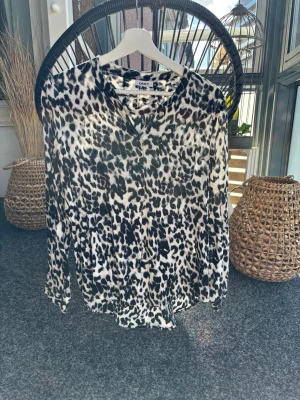Leopardfärgad blus - Supermjuk leopardblus med knappar fram och ficka över vänster bröst. Viskos, strykfri. Beige botten, svarta leopardfläckar.