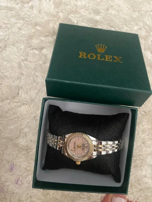 Silverfärgad klocka med rosa bo med gulddetaljer - Stilren klocka med länkarmband i silverfärg och gulddetaljer. Klassisk design med metallarmband som ger en lyxig känsla. Perfekt accessoar för dig som gillar en elegant look.