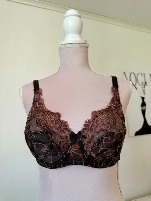 Svart spets-bh med bruna broderier - Säljer en elegant svart bh med vackra bruna broderade blommor och meshdetaljer. i storlek 80B med stretchig band som är 69cm. Ärmarna är tjocka band och är justerbara💕 Ny utan prislapp . Bh:n har reglerbara axelband och en liten rosett framtill. Materialet är genomskinlig mesh och spets som ger en lyxig känsla. 