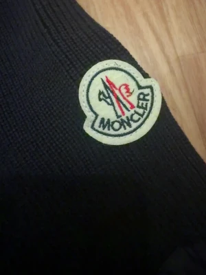 Marinblå stickad pufferjacka Moncler - Snygg marinblå pufferjacka från Moncler med stickade ärmar och quiltade partier. Jackan har en dragkedja på ärmen och det klassiska Moncler-märket på armen. Perfekt för dig som vill ha en stilren och exklusiv look.