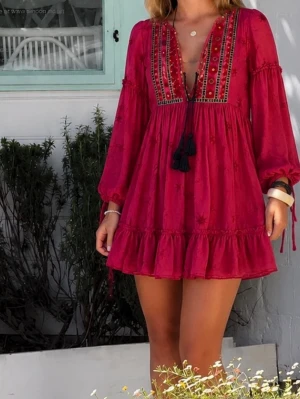 Röd boho kortklänning med volang - Snygg röd kortklänning i boho-stil med volangkant, broderade detaljer och snörning framtill. Klänningen har långa ärmar och v-ringad halsringning med dekorativa tofsar. Perfekt för sommarens alla tillfällen.