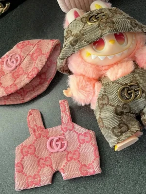 Labubu + gg kläder  - Labubu med 2 set tillhörande lyxiga kläder ✨.                                 Hängselbyxor + hatt i rosa och brunt med kända loggan. Väldigt bra kvalité! (Säljer endast allt tillsammans) 