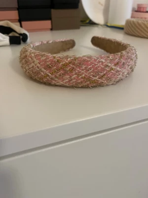 Rosa tweeddiadem med guldtråd - Supersött diadem i rosa och vitt tweedtyg med inslag av glittrig guldtråd. Bred och vadderad modell som ger en trendig look. Perfekt accessoar för att lyfta din outfit med en touch av lyxig känsla.