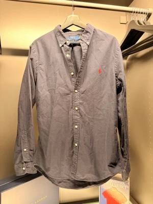Ralph Lauren - Klassisk mörkblå skjorta från Ralph Lauren i slim fit med knappar framtill och på kragen. Skjortan har lång ärm och den ikoniska röda logotypen broderad på bröstet. Tillverkad i mjuk bomull som känns skön mot huden.
