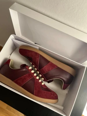 Maison margiela gats skor vinröd - Snygga sneakers i vinrött mocka och läder med beige snörning och gummisula. Klassisk låg modell med retrovibbar och stilren design. Perfekta för dig som vill ha något unikt och trendigt till vardagslooken. Använda 2 gånger, box och dustbag ingår ej.