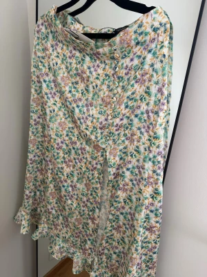 Blommig långkjol från Zara - Säljer en blommig långkjol från Zara i ljusa färger med inslag av grönt, lila och gult. Kjolen har knappar framtill och ett flowigt fall. Perfekt för vår och sommar när du vill ha en romantisk look.