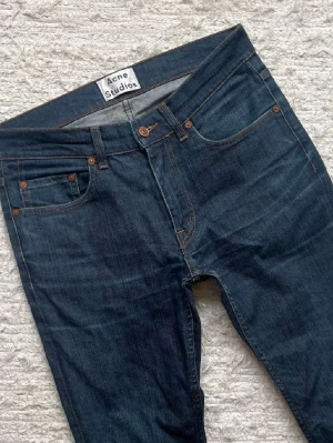 Mörkblå Acne Studios jeans - Säljer ett par mörkblå jeans från Acne Studios med klassisk femficksmodell och smal passform. De är i storlek W30 L32. Jeansen har snygga kopparfärgade nitar och kontrastsömmar. Perfekta för dig som gillar stilrena och tidlösa jeans i hög kvalitet. Det är bara att höra av sig vid minsta fundering🙌