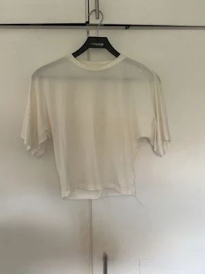 Vit croppad t-shirt i bomull - En enkel vit croppad t-shirt med rund hals och korta ärmar. Tillverkad i mjuk bomull som känns skön mot huden. Perfekt till jeans eller kjol för en avslappnad look.