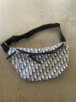 Superfin väska❤️ - Säljer en snygg shoppingväska  med klassiskt svartvitt monogrammönster. Väskan har två dragkedjefack med guldfärgade detaljer och justerbart svart band. Perfekt för dig som vill ha en trendig och praktisk accessoar.