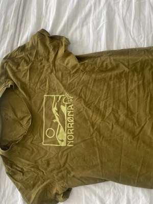 Grön t-shirt från Norrøna - Snygg grön t-shirt från Norrøna med tryck av berg och sol på bröstet. Klassisk passform och rund halsringning. Perfekt för dig som gillar outdoor.