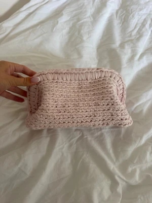 Ljusrosa virkad clutch - Supersöt egengjord ljusrosa clutch i virkat material. Väskan har en mjuk, rektangulär form och är perfekt för småprylar eller smink. Ger en mysig och trendig känsla till din look.