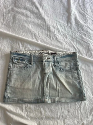 Ljusblå jeanskjol från Denim by Stradivarius - Supersnygg ljusblå jeanskjol från Denim by Stradivarius. Kort modell med klassiska fickor fram och bak, knapp- och dragkedjestängning samt slitna detaljer för en cool vibe. Perfekt till sneakers eller boots för en trendig look.