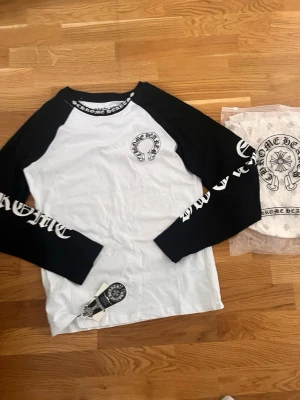 Chrome Hearts långärmad t-shirt - Säljer en långärmad t-shirt från Chrome Hearts med svartvita kontraster. Tröjan har svart text och logga på bröstet, tryck längs ärmarna och runt halsen. Klassisk baseballmodell i bomull med cool streetwear-vibe.