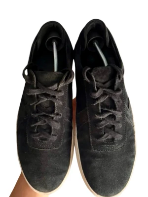 Axel Arigato svarta mockasneakers (43) - Stilrena svarta sneakers i mocka från Axel Arigato med klassisk låg profil och vit, tjock gummisula. Skorna har svarta skosnören och diskreta sömmar för en clean look. Perfekta för dig som gillar minimalistisk stil och vill ha något som funkar till det mesta.