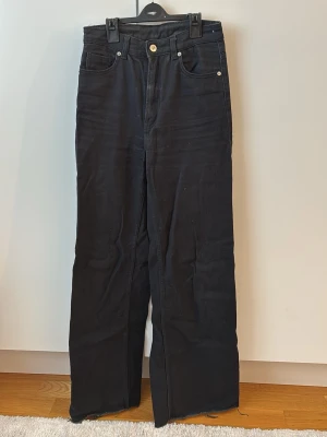 Svarta raka jeans från H&M - Säljer ett par svarta jeans från H&M i storlek 34. Jeansen har hög midja, raka ben med lätt utsvängd passform och slitna kanter nertill. Gåva vid köp!🎁