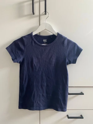 Mörkblå ribbad t-shirt från 157 - En enkel och stilren mörkblå ribbad t-shirt från 157. Perfekt till jeans eller shorts för en clean look. 1 litet hål ca 1 cm i sömmen på en kant vi halsen, enkelt fix! Den är sparsamt använd! Skriv privat för mer information/bilder!